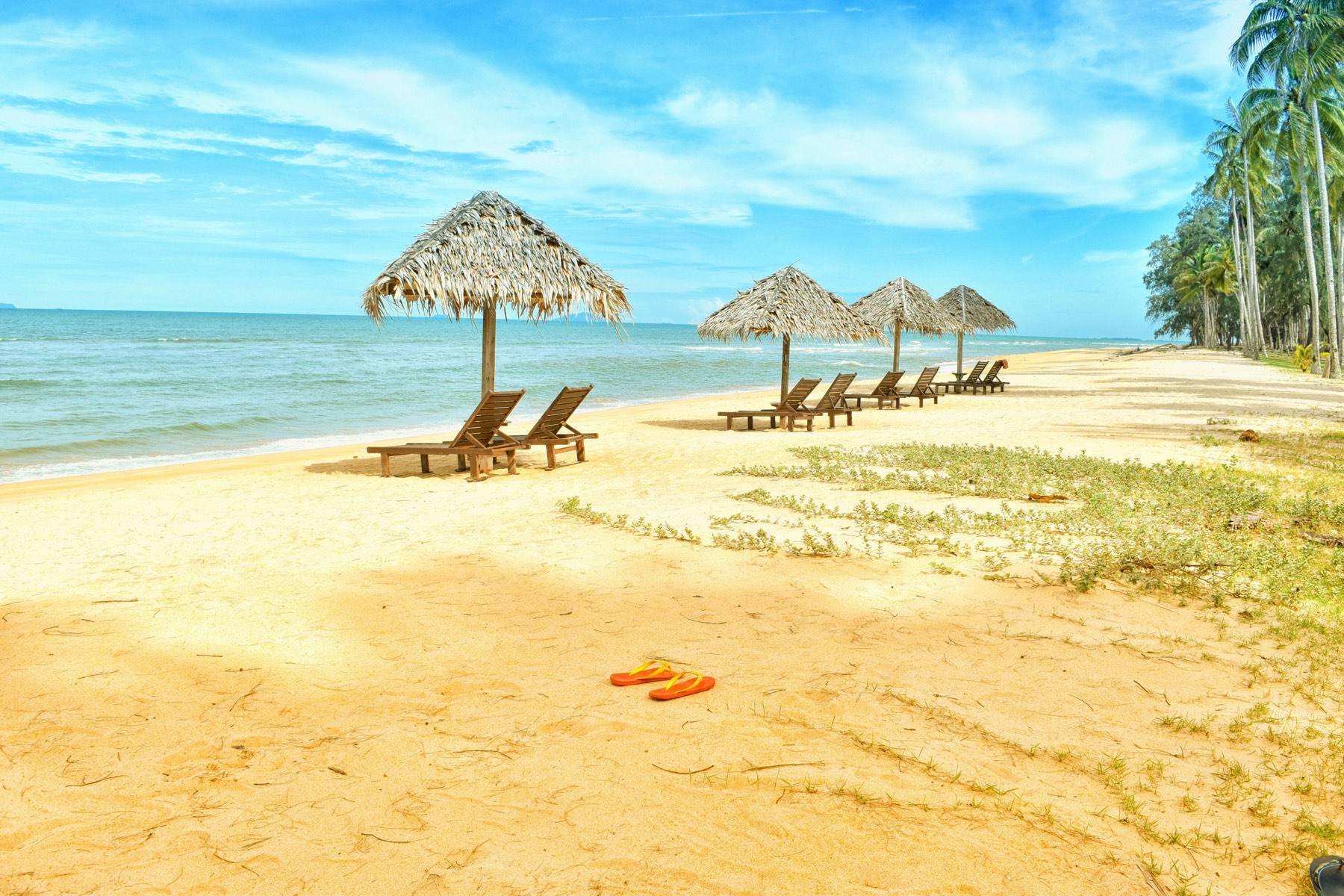 Strand mit Sonnenliegen und Palmen am Meer